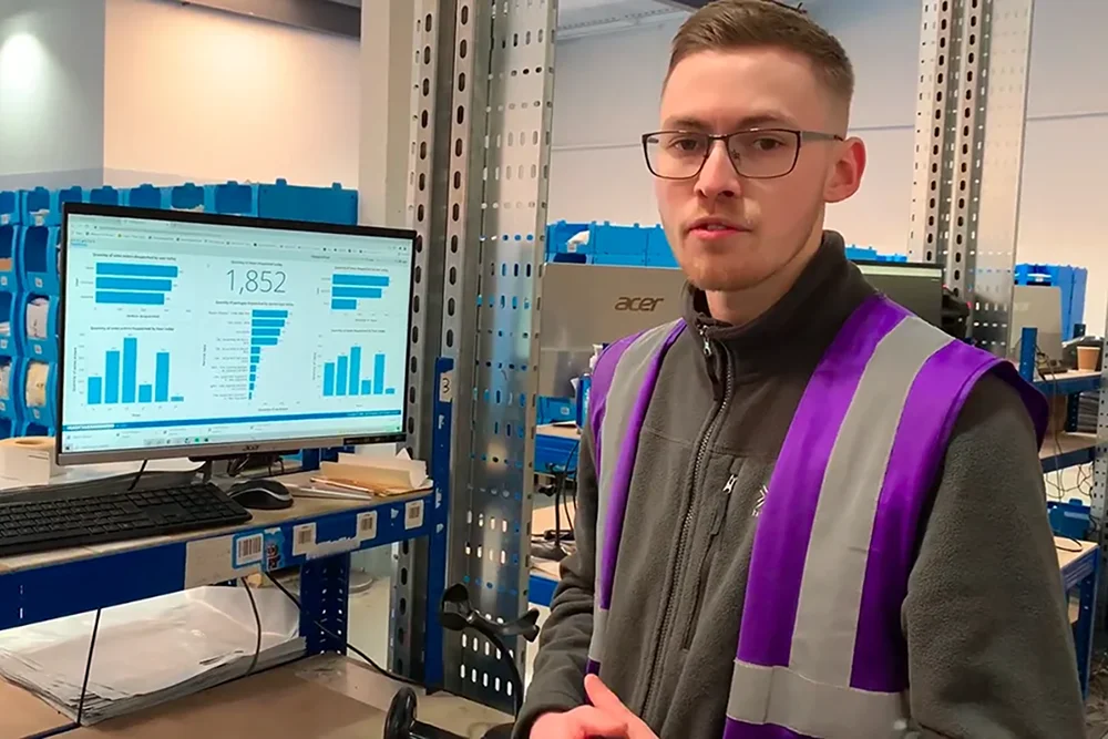 A warehouse operations manager in a warehouse has key performance metrics dashboard displayed on a computer monitor