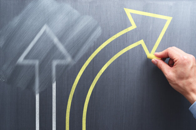 Hand draws arrow symbolizing exploring a different path on a chalkboard