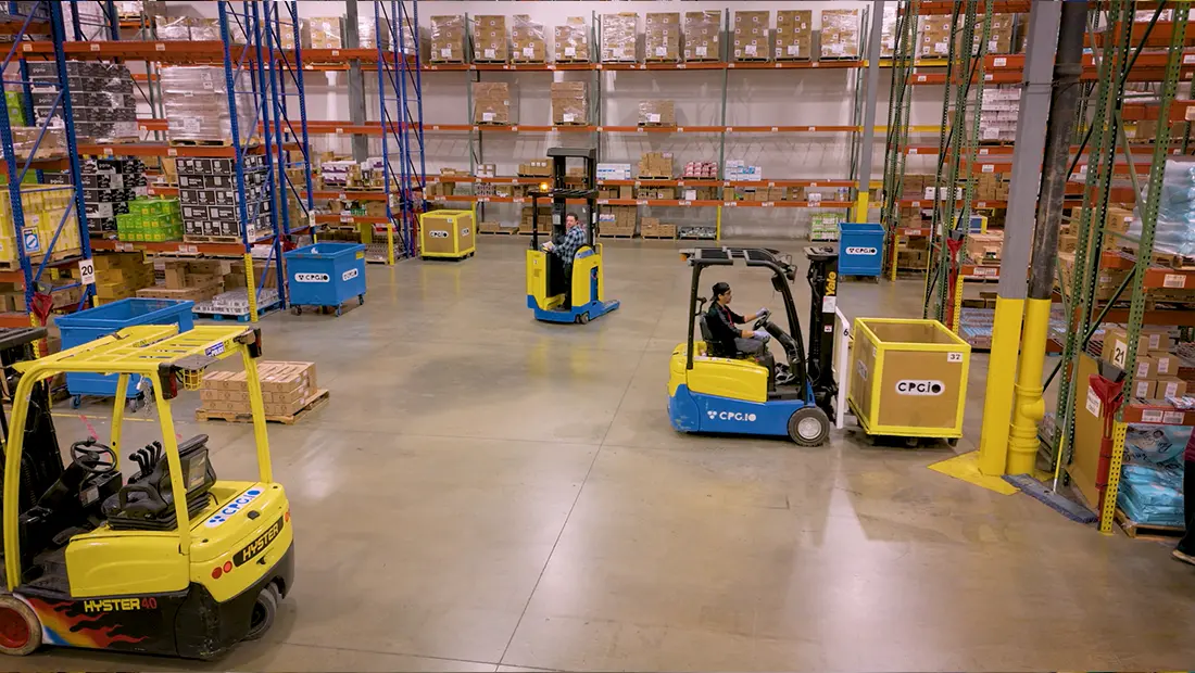 An image from the CPGIO warehouse. It shows CPGIO-branded forklifts; two are being driven.
