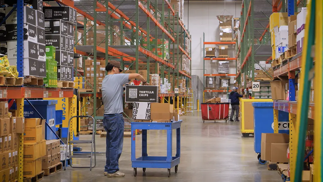 An image of a CPGIO warehouse worker picking order items and placing them on a trolley.