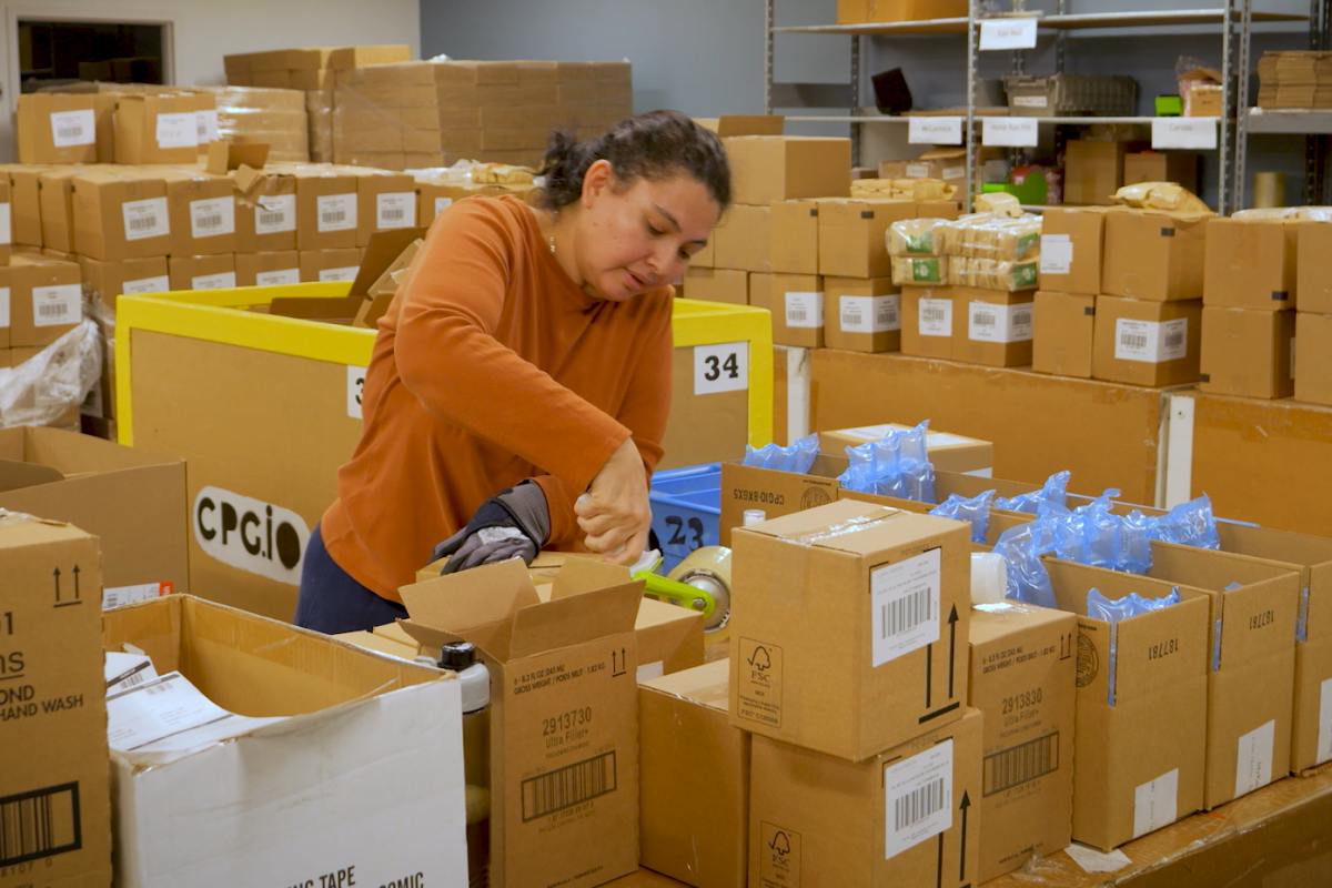 Worker taping a parcel and fulfilling orders in a large ecommerce warehouse full of boxes
