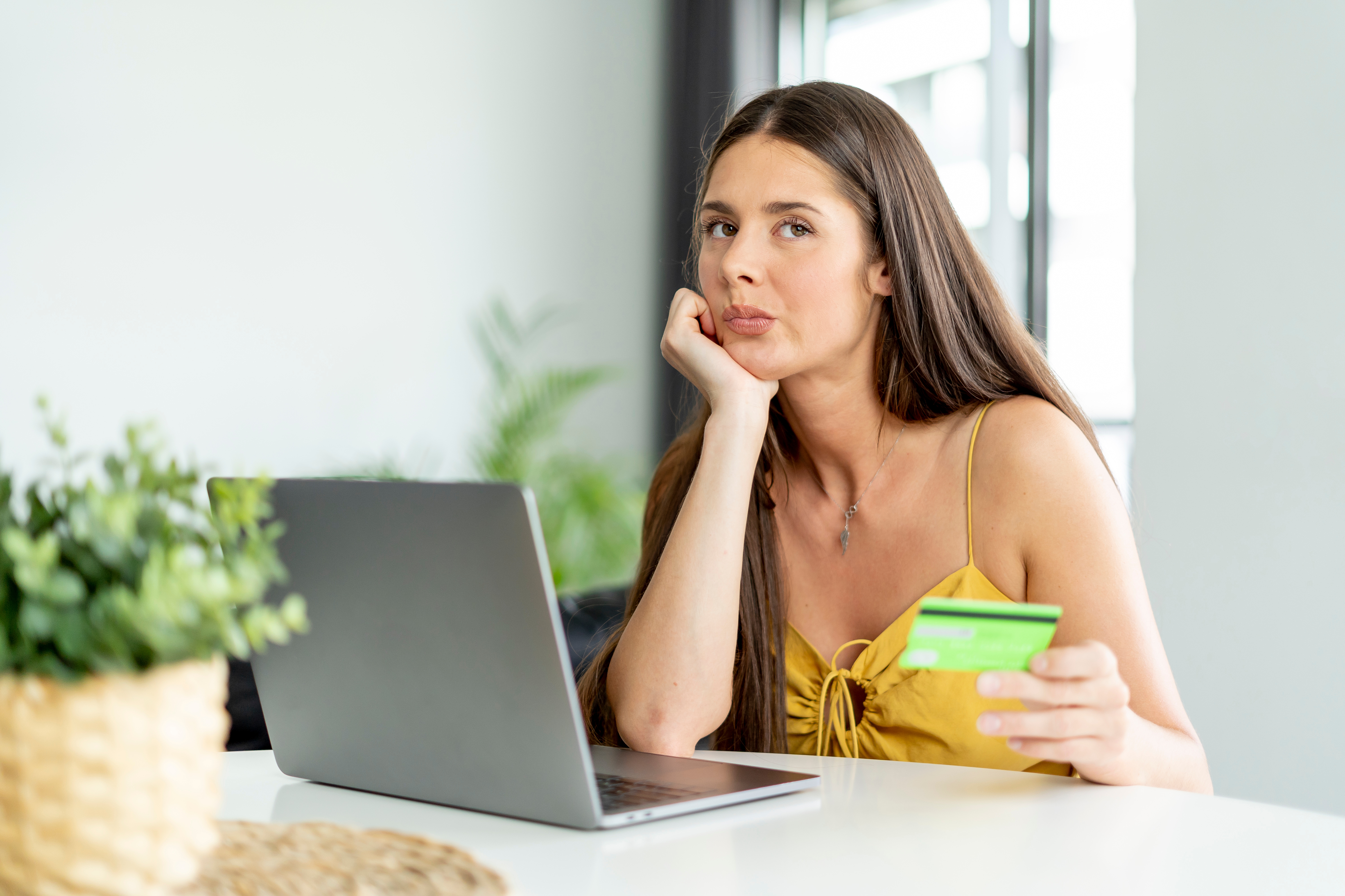 An image showing an online shopper sitting in front of a laptop and holding a credit card. She looks uncertain about whether she wants to go through with the purchase.