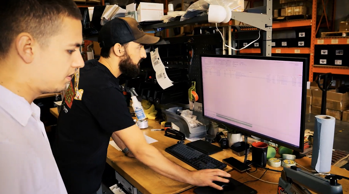 Owner David Rajewski and a Descartes representative review order and inventory data on a computer in the warehouse workspace.