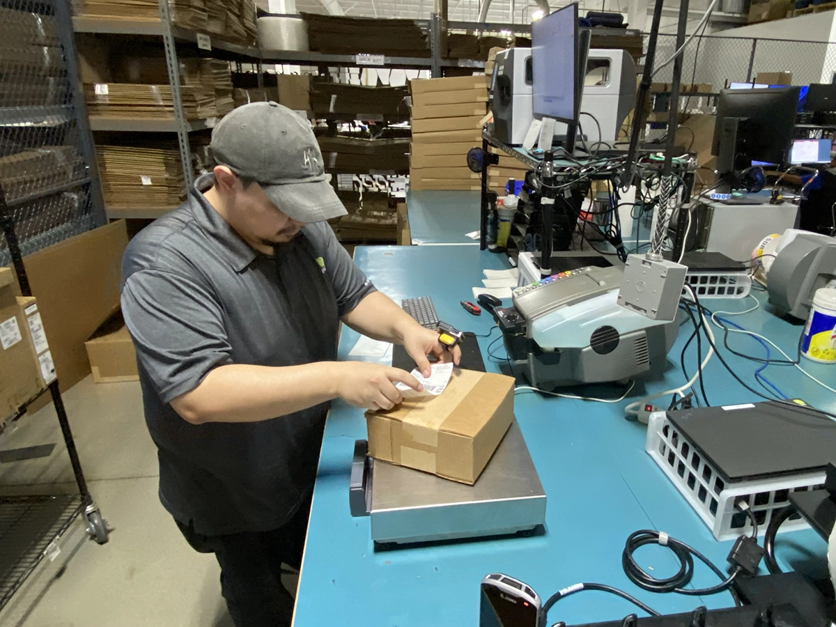 Shipping station worker applying label to parcel on scale
