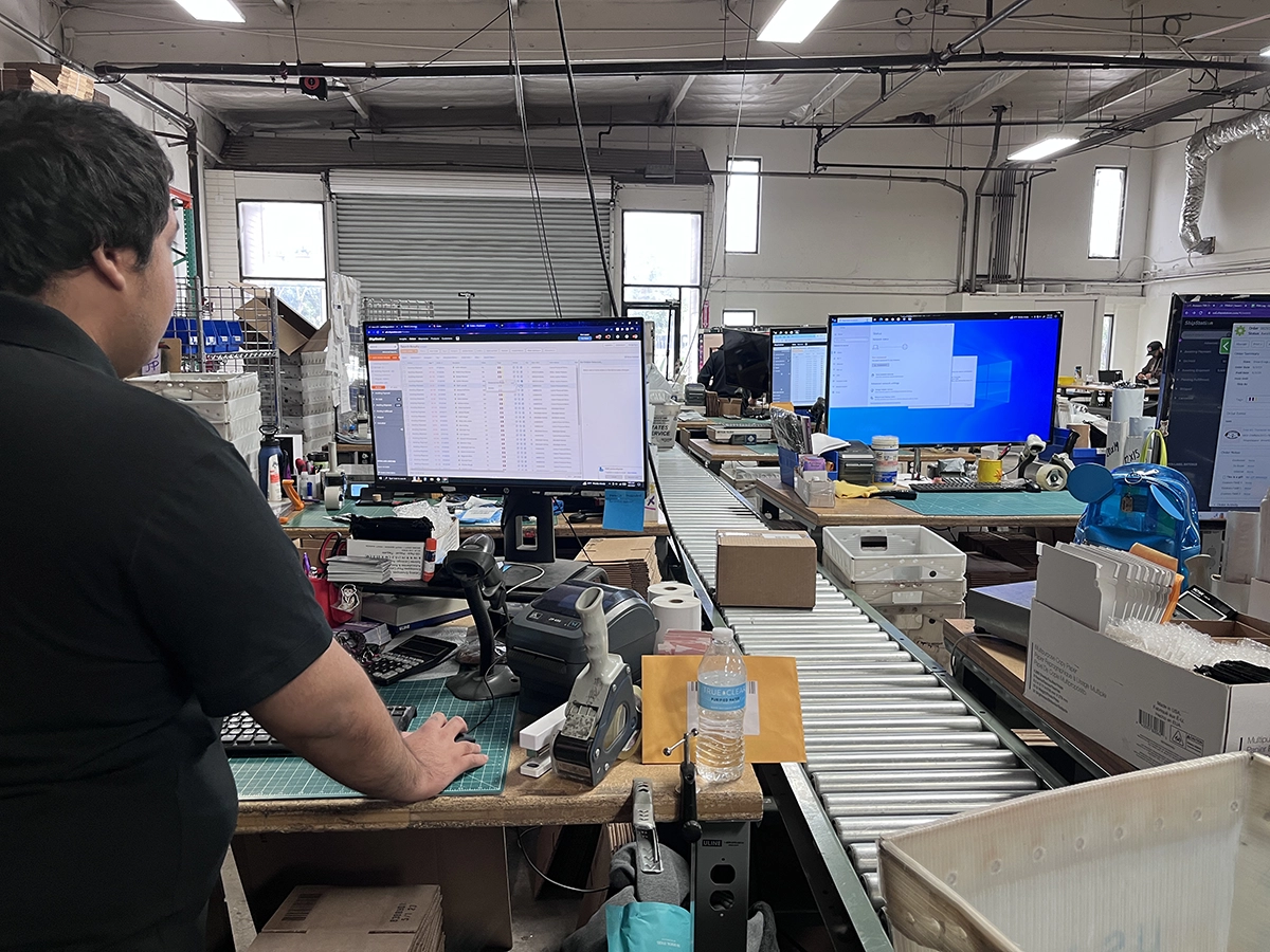 Warehouse worker using Descartes Finale inventory software to fulfill orders at a shipping station