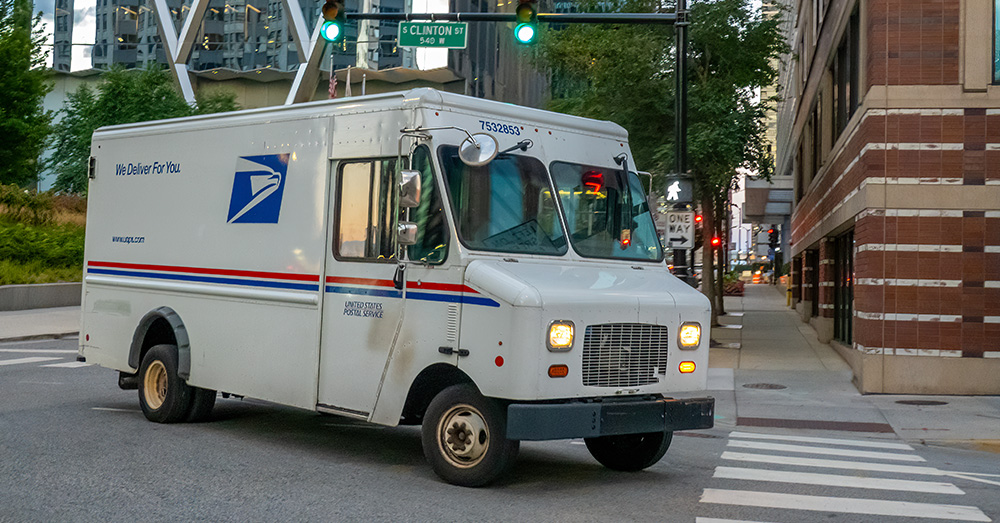 An image of a USPS delivery truck turning down a street.