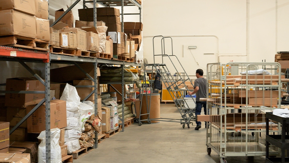Warehouse worker navigating aisles with inventory shelves, boxes, and stock materials in a storage facility