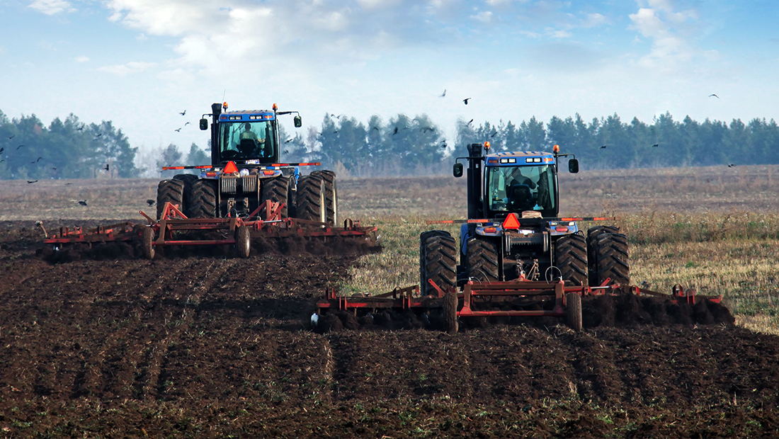 A farm field is being tilled by a team of two large tractors
