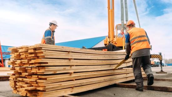 Two workers unload lumber from crane at construction site