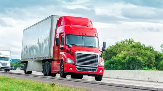 Horizontal shot of a red eighteen wheeler traveling down an interstate highway