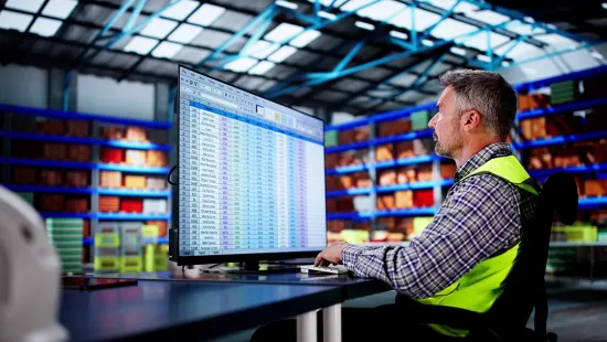 Warehouse worker using a computer with a large spreadsheet for inventory forecasting