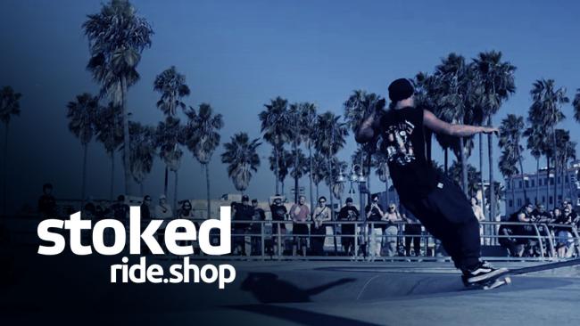 Skateboarder performing a trick at a skate park with palm trees in the background and the Stoked Ride Shop logo displayed on screen.