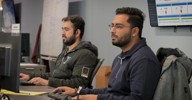 An image of two office workers sitting at their workstations.