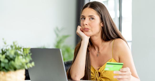 An image showing an online shopper sitting in front of a laptop and holding a credit card. She looks uncertain about whether she wants to go through with the purchase.