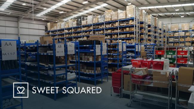 Wide view of the Sweet Squared warehouse with organized storage racks, picking stations, boxes, and inventory bins. 