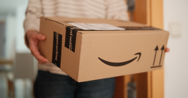 An image of someone holding an Amazon order. The package features the Amazon smile and Amazon Prime tape is used to seal the box.