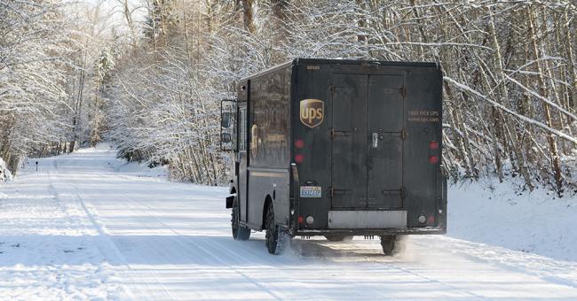 UPS delivery truck drives down a snow-covered road lined with trees.